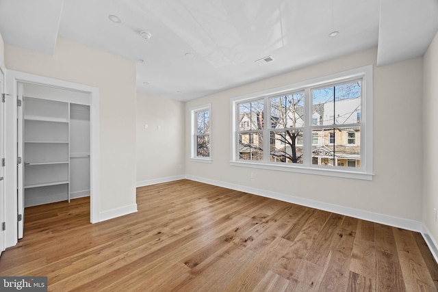 unfurnished bedroom with visible vents, baseboards, a closet, a walk in closet, and light wood-type flooring