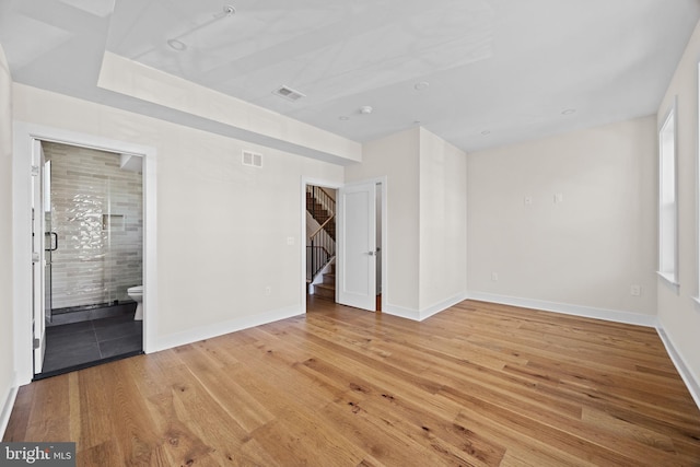 empty room featuring stairs, wood finished floors, visible vents, and baseboards