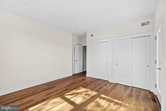 unfurnished bedroom with wood finished floors, visible vents, two closets, and baseboards