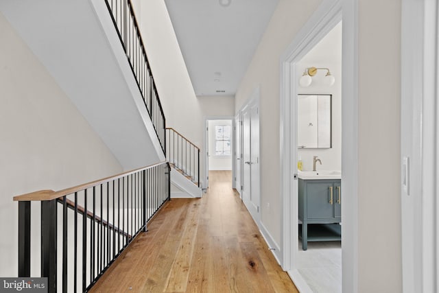 hallway with a sink, stairway, and light wood-style floors