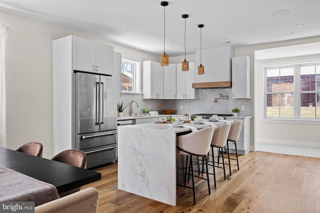 kitchen featuring a sink, a kitchen breakfast bar, light wood finished floors, decorative backsplash, and high end refrigerator