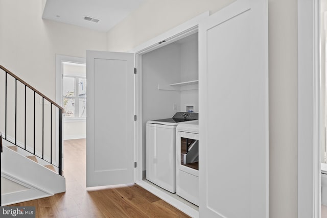 clothes washing area with laundry area, wood finished floors, visible vents, and washer and clothes dryer