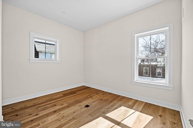 empty room with plenty of natural light, baseboards, and wood-type flooring