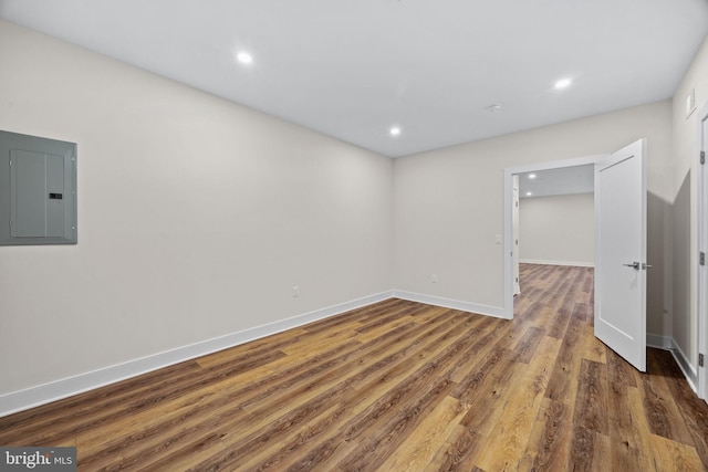 empty room with electric panel, recessed lighting, baseboards, and wood finished floors