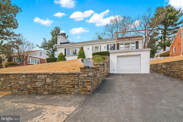 view of front of property featuring driveway, a chimney, and a balcony