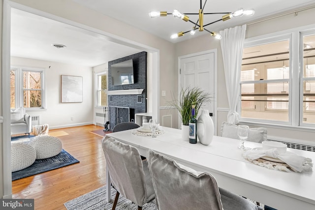 dining room featuring visible vents, baseboards, a fireplace, light wood-style floors, and a notable chandelier