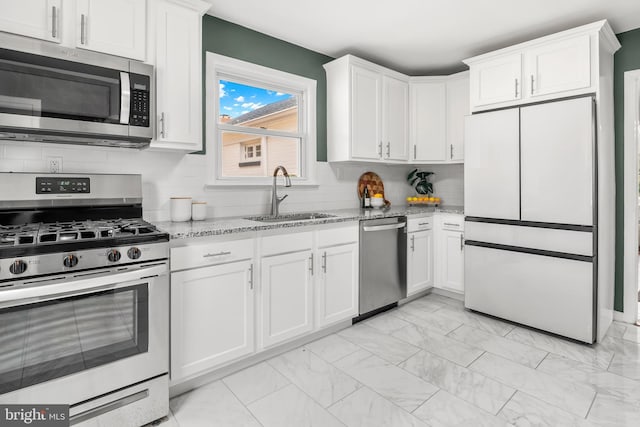 kitchen featuring white cabinetry, light stone counters, appliances with stainless steel finishes, and a sink