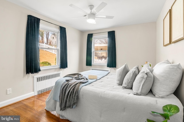 bedroom with baseboards, multiple windows, wood finished floors, and radiator heating unit