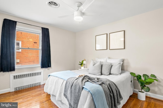 bedroom featuring visible vents, multiple windows, radiator, and wood finished floors