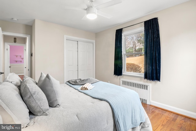 bedroom with radiator, ceiling fan, baseboards, wood finished floors, and a closet