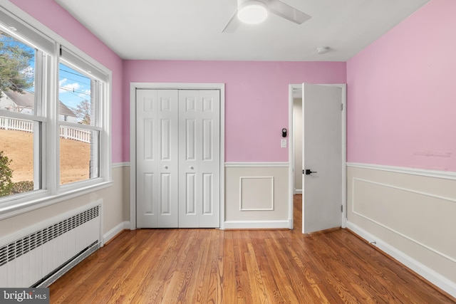 unfurnished bedroom featuring a closet, a wainscoted wall, light wood-style flooring, and radiator heating unit