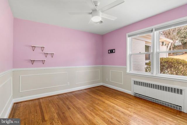 unfurnished room featuring plenty of natural light, radiator heating unit, a wainscoted wall, and wood finished floors