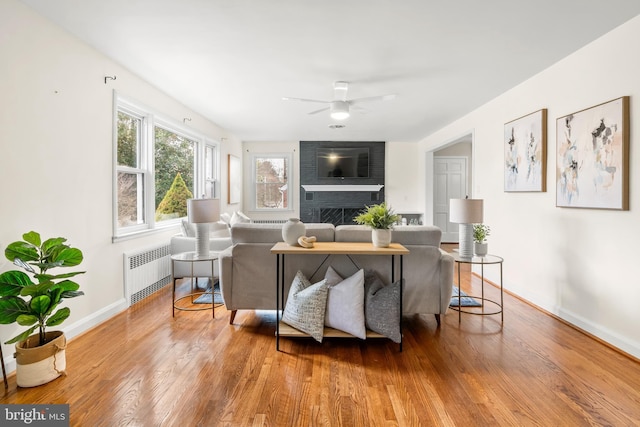 living room with radiator, a ceiling fan, wood finished floors, baseboards, and a fireplace