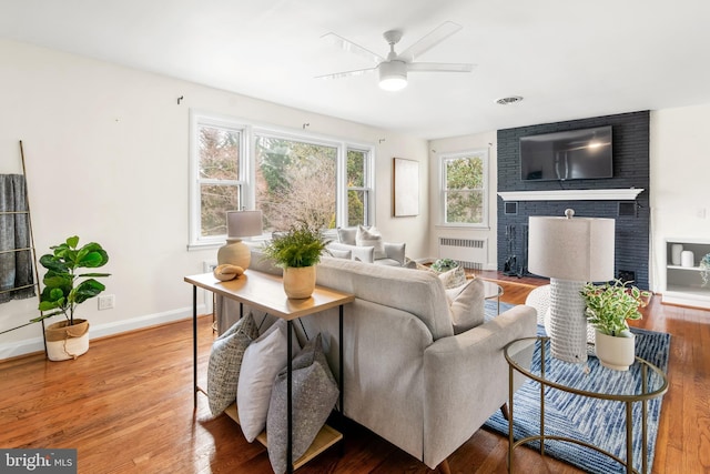 living room featuring ceiling fan, wood finished floors, a fireplace, and radiator heating unit