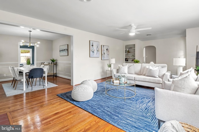 living area featuring ceiling fan with notable chandelier, built in shelves, wood finished floors, and arched walkways