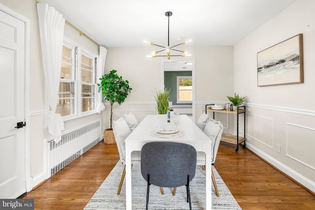 dining space with a wainscoted wall, radiator, an inviting chandelier, and wood finished floors