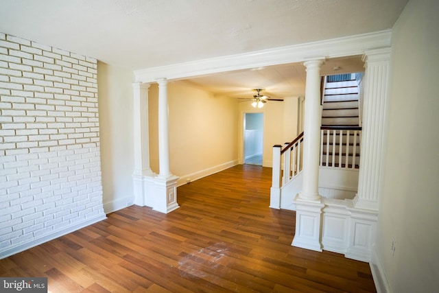 spare room with a ceiling fan, brick wall, wood finished floors, and ornate columns