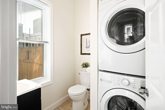 clothes washing area featuring tile patterned floors, stacked washer / drying machine, and baseboards