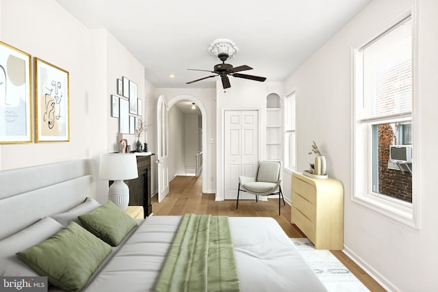 bedroom featuring wood finished floors, baseboards, arched walkways, ceiling fan, and a closet