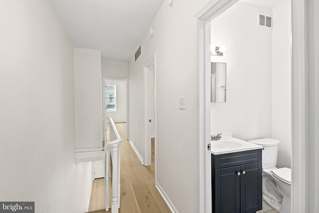 corridor with visible vents, light wood-type flooring, baseboards, and a sink