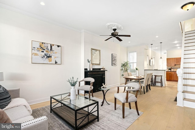 living room featuring ornamental molding, stairway, light wood-style floors, baseboards, and ceiling fan