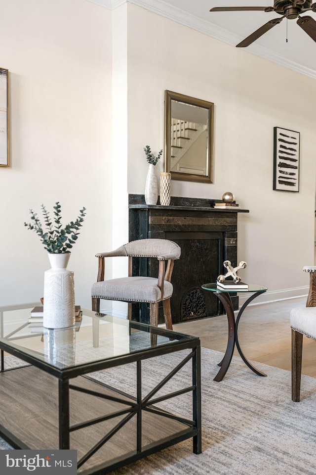 sitting room with ceiling fan, baseboards, wood finished floors, and crown molding