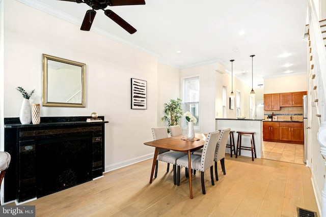 dining area featuring baseboards, visible vents, light wood finished floors, and ornamental molding