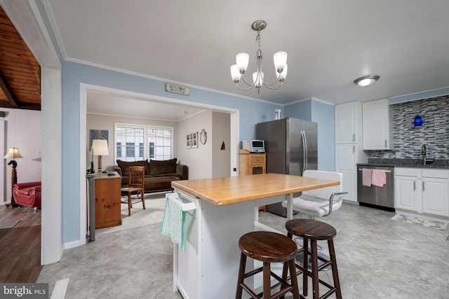 kitchen featuring crown molding, a breakfast bar, decorative backsplash, appliances with stainless steel finishes, and white cabinetry