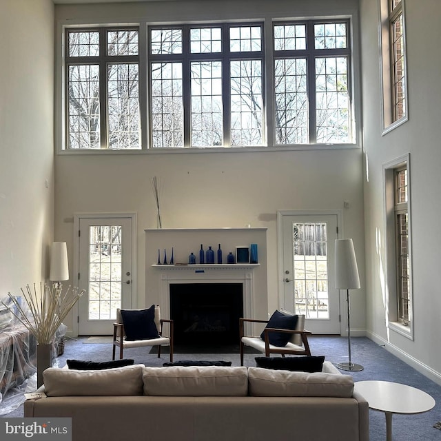 living room with carpet floors, a healthy amount of sunlight, a towering ceiling, and a fireplace with flush hearth