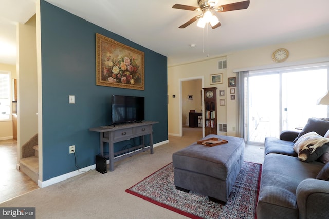 carpeted living room featuring visible vents, baseboards, ceiling fan, and stairway