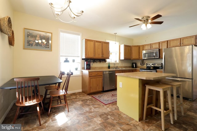 kitchen with baseboards, hanging light fixtures, light countertops, appliances with stainless steel finishes, and a center island