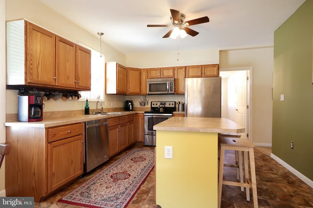 kitchen with a ceiling fan, a sink, decorative light fixtures, a center island, and appliances with stainless steel finishes