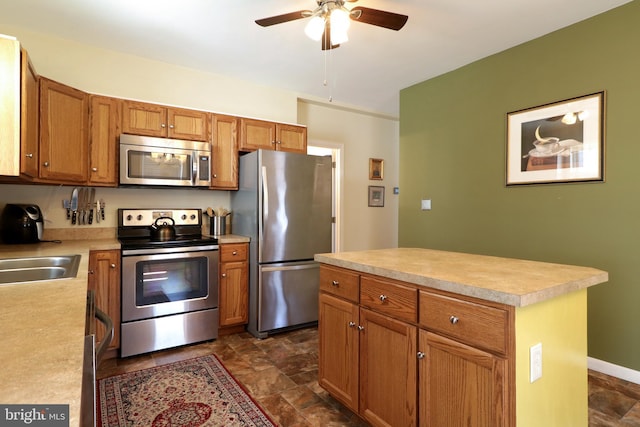 kitchen featuring a kitchen island, light countertops, appliances with stainless steel finishes, brown cabinetry, and a sink