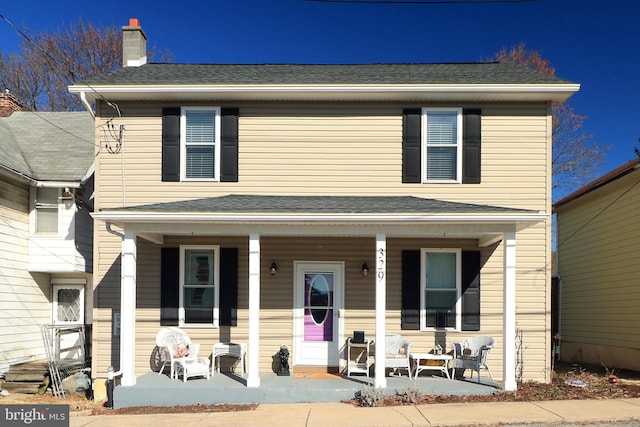 view of front of property featuring a chimney, a porch, and a shingled roof