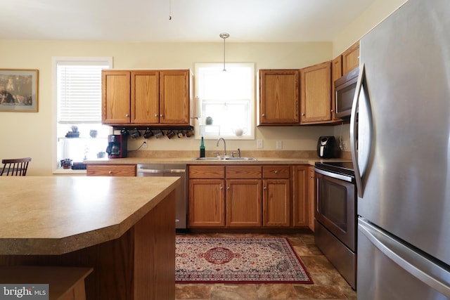 kitchen featuring brown cabinets, pendant lighting, a sink, appliances with stainless steel finishes, and light countertops