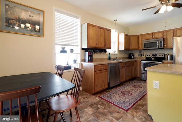 kitchen with light countertops, appliances with stainless steel finishes, hanging light fixtures, stone finish floor, and a sink