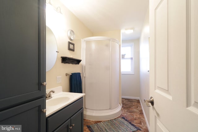 bathroom featuring a stall shower, vanity, stone finish flooring, and baseboards