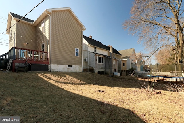 rear view of property with a yard, a trampoline, and a deck