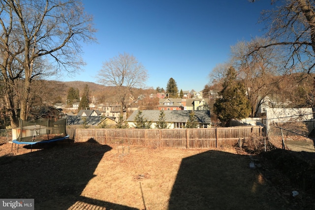 view of yard featuring a trampoline, fence, and a residential view