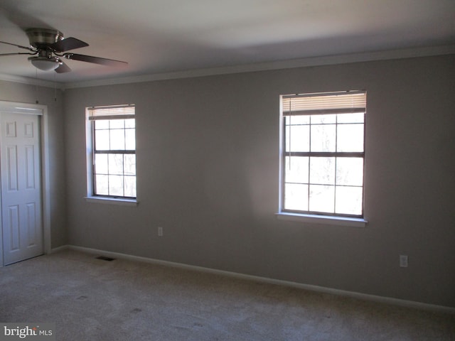 empty room featuring visible vents, baseboards, crown molding, and carpet