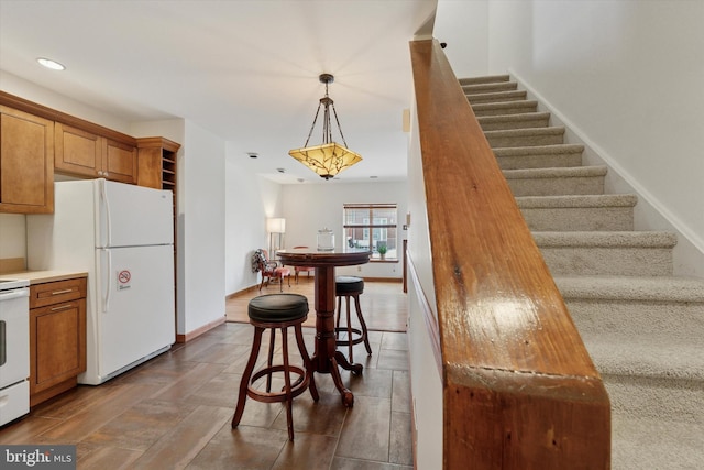 kitchen with hanging light fixtures, white appliances, brown cabinetry, and baseboards