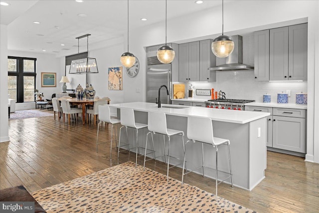 kitchen with stainless steel built in refrigerator, wall chimney exhaust hood, light wood-type flooring, and a sink