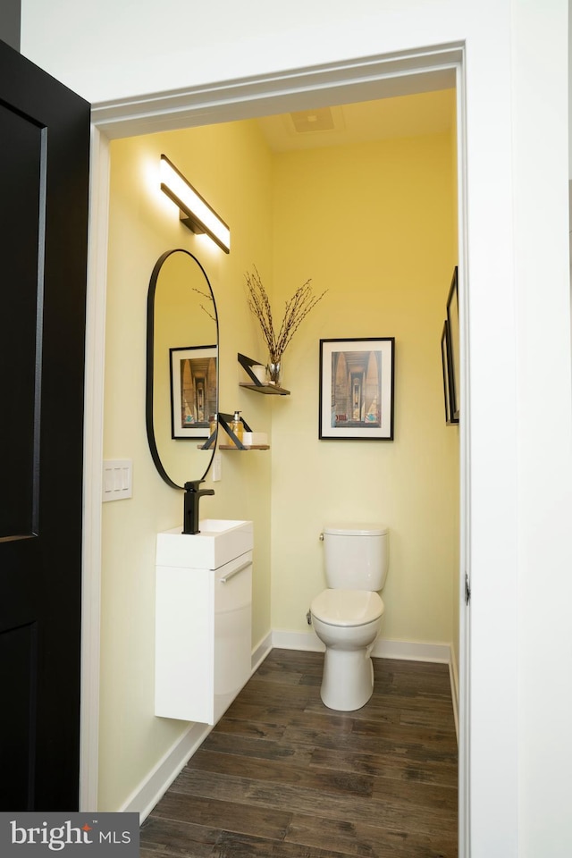 half bathroom with toilet, vanity, baseboards, and wood finished floors