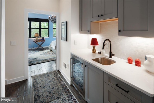 kitchen with dark wood-type flooring, gray cabinetry, a sink, tasteful backsplash, and light countertops