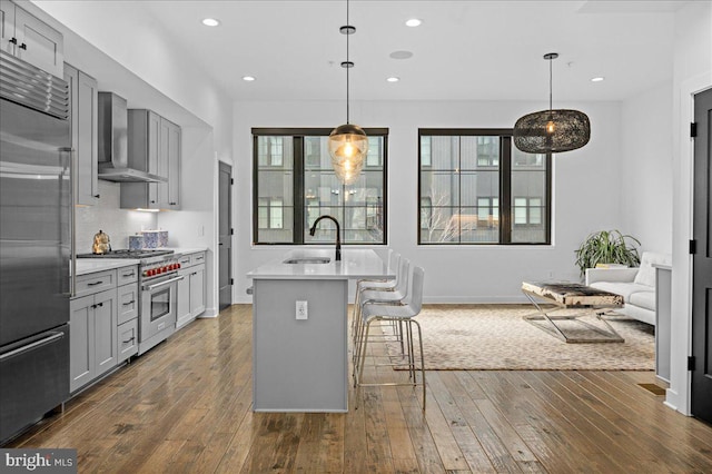 kitchen with light countertops, gray cabinets, wall chimney exhaust hood, high end appliances, and a sink