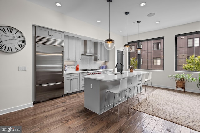 kitchen featuring a sink, gray cabinetry, light countertops, stainless steel appliances, and wall chimney range hood