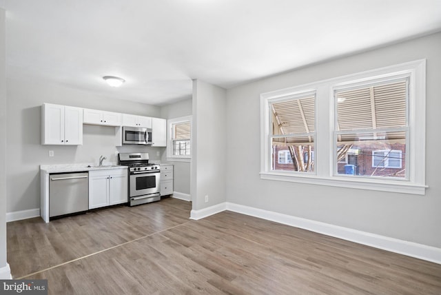 kitchen with a sink, stainless steel appliances, baseboards, and white cabinetry