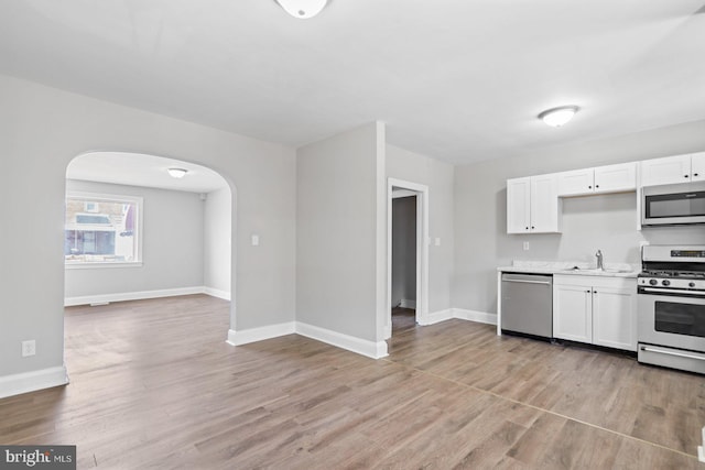 kitchen with light wood finished floors, arched walkways, stainless steel appliances, light countertops, and white cabinets