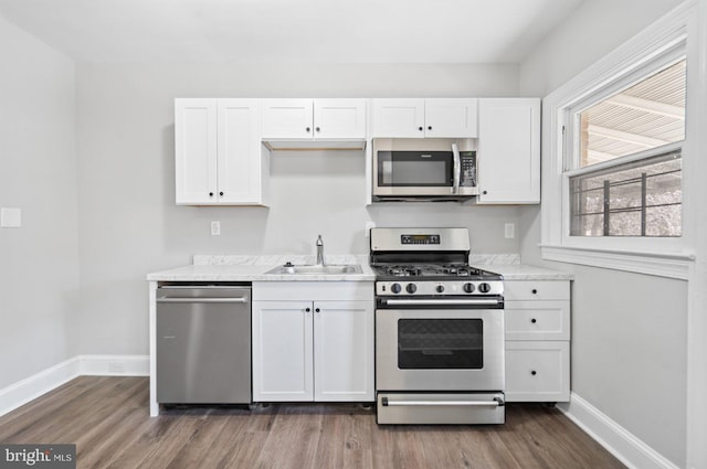 kitchen featuring dark wood-style floors, baseboards, a sink, appliances with stainless steel finishes, and white cabinetry