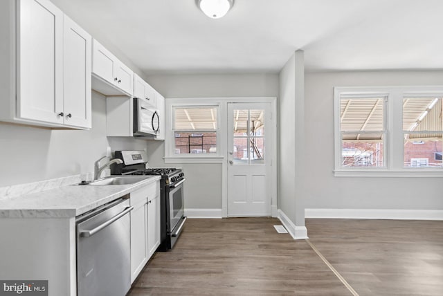 kitchen with appliances with stainless steel finishes, white cabinetry, light countertops, and wood finished floors